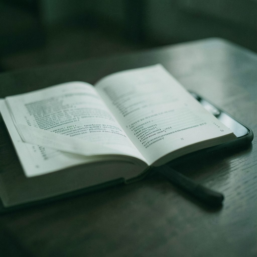 A narrow vertical cover-style image of an open programming book beside a smartphone, dark green and white tones, quiet studious mood